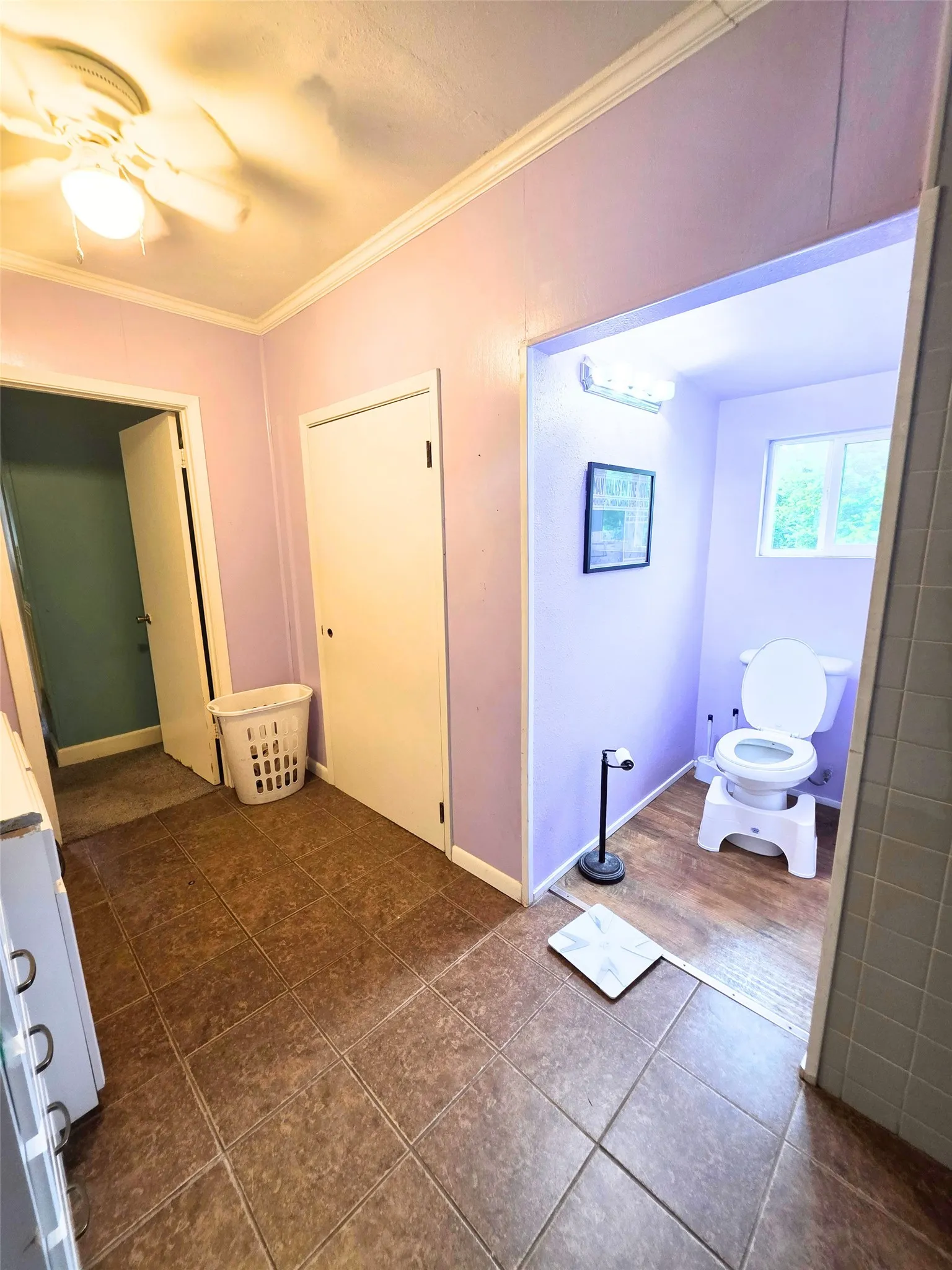 Tile flooring extending into a separate commode area featuring a window and wall-mounted lighting