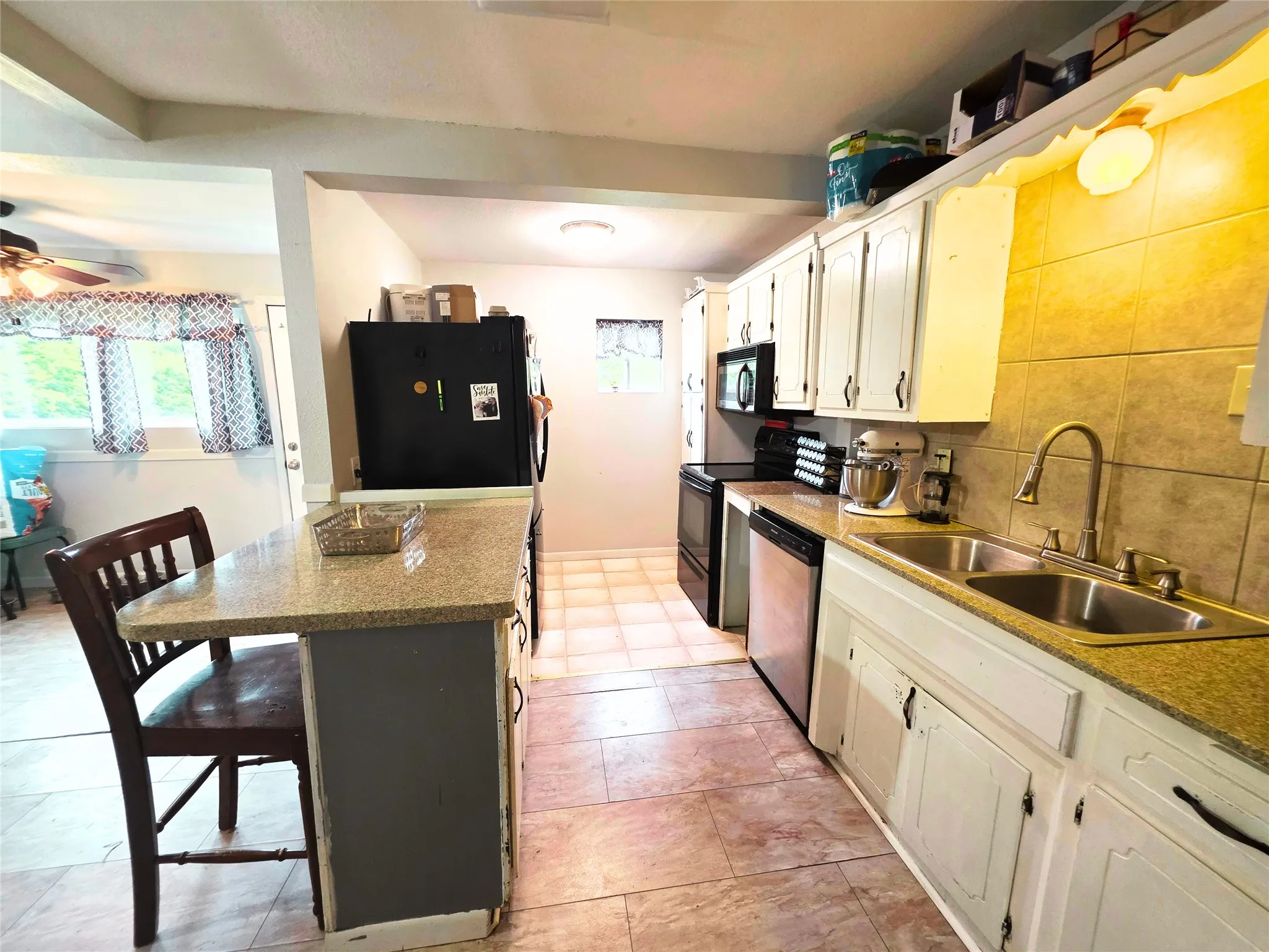 Kitchen featuring an extended island with a stone-finish countertop, an integrated double-basin stainless steel sink, tile backsplash, and matching tile flooring
