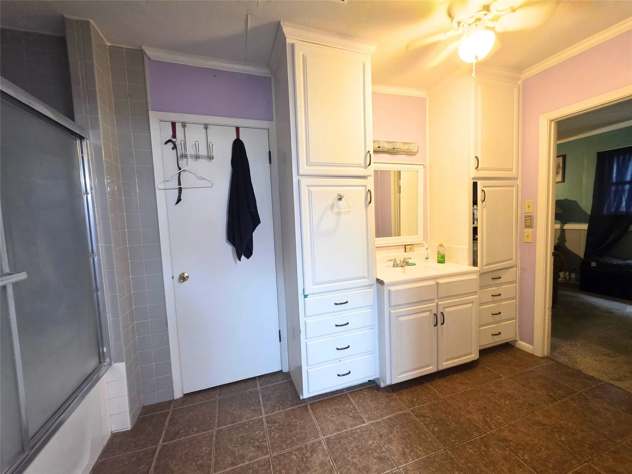 Bathroom featuring a white vanity with integrated sink, extensive white cabinetry, a shower with sliding glass doors, and brown tile flooring