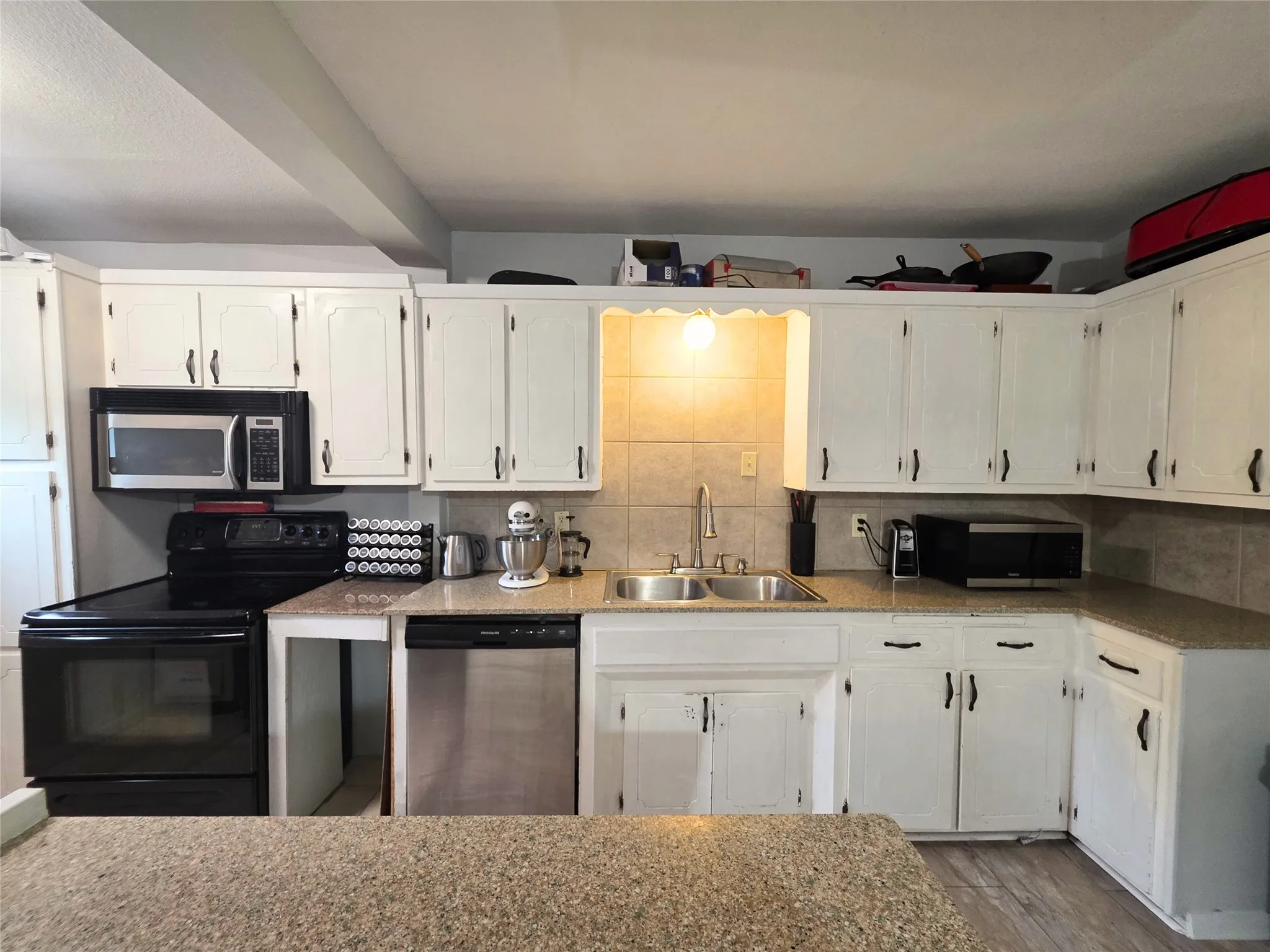 Kitchen featuring white cabinetry, light-colored countertops, dual basin sink with gooseneck faucet, tile backsplash, and stainless steel dishwasher