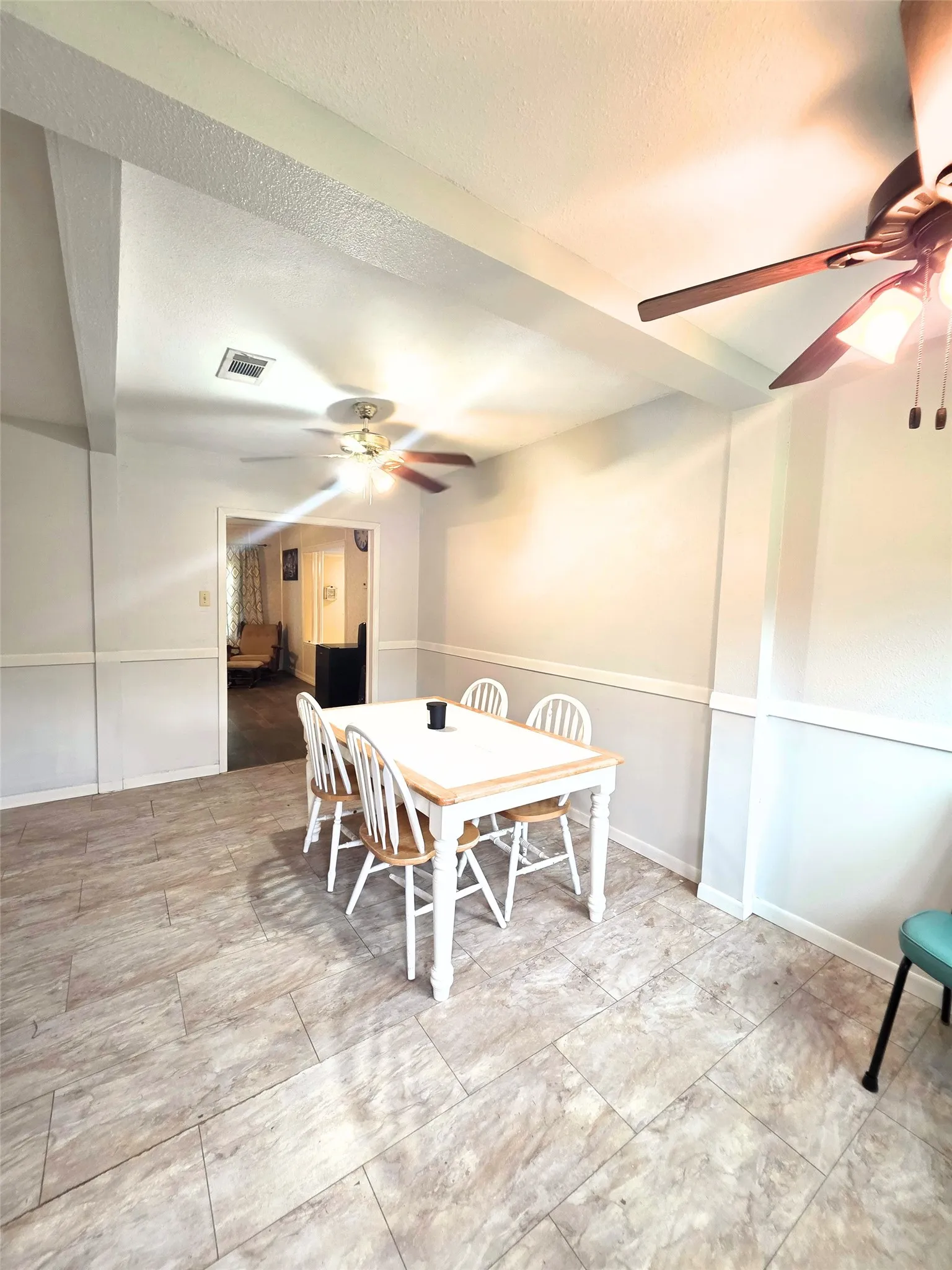 Spacious interior room featuring tile flooring, ceiling fans, and a partial wainscoting wall treatment