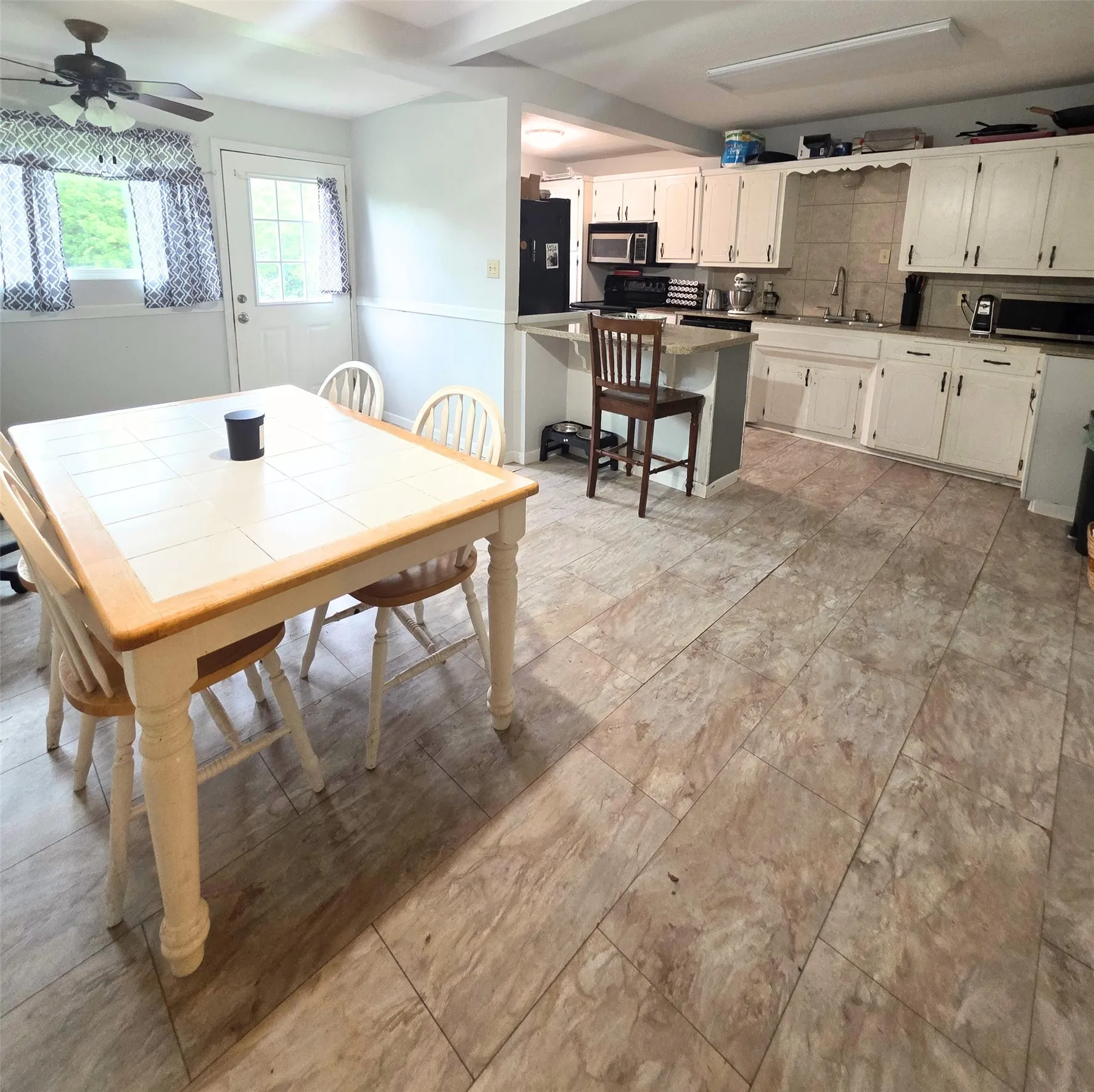 Open-concept kitchen and dining area featuring light-toned flooring, white cabinetry, a black refrigerator, and a kitchen island with a dark countertop