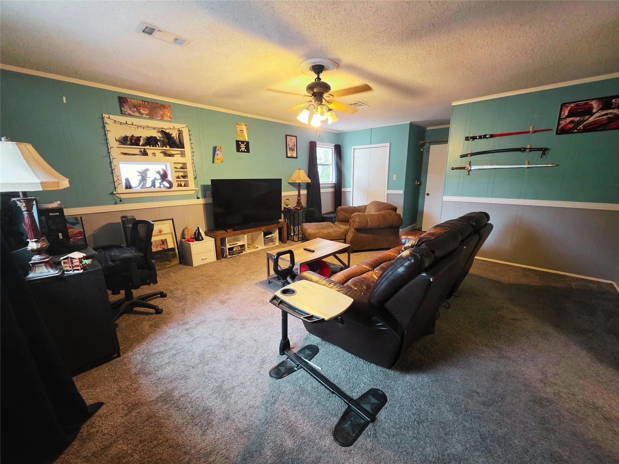 Spacious interior room featuring a textured ceiling with a ceiling fan, light-colored carpeting, two-tone wall paneling, and white trim