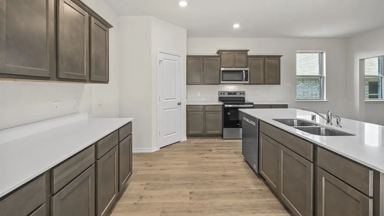 Spacious kitchen featuring an expansive island with a double basin sink, stainless steel appliances, ample cabinetry, and light wood-finish flooring