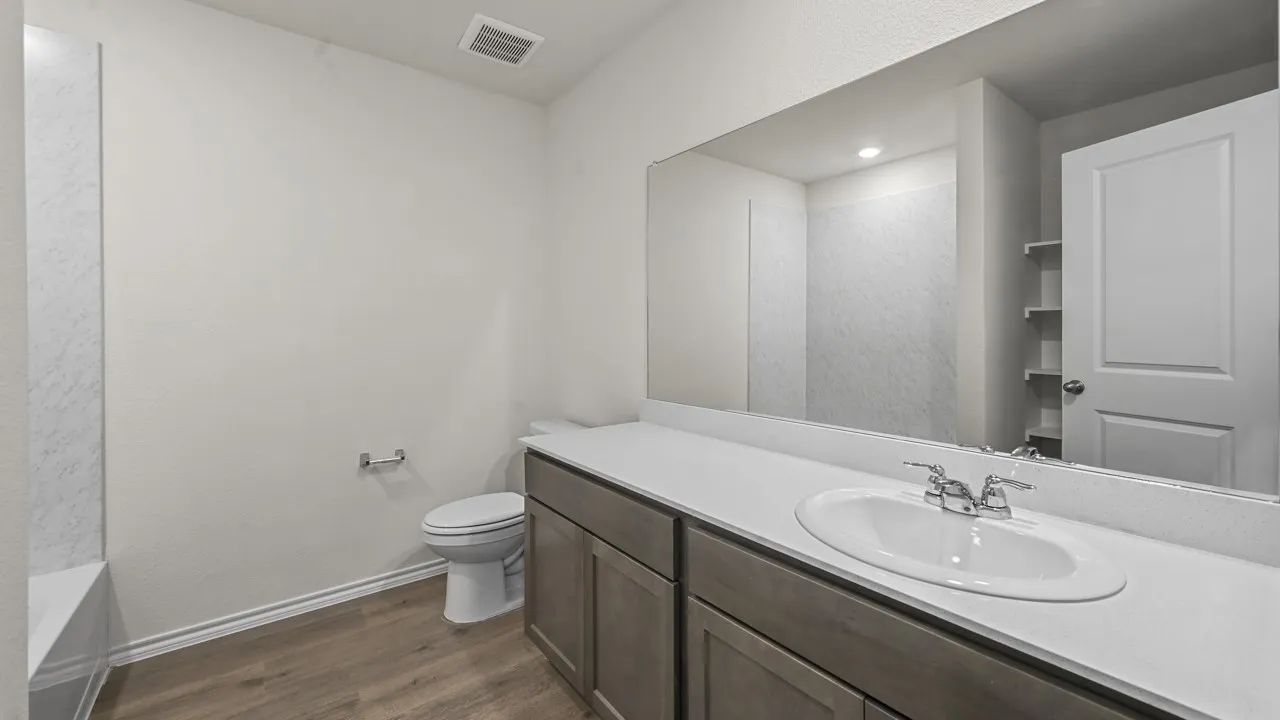 Bathroom featuring a wood-finish vanity with a single basin sink, extensive countertop space, a large wall-mounted mirror, and wood-finish flooring