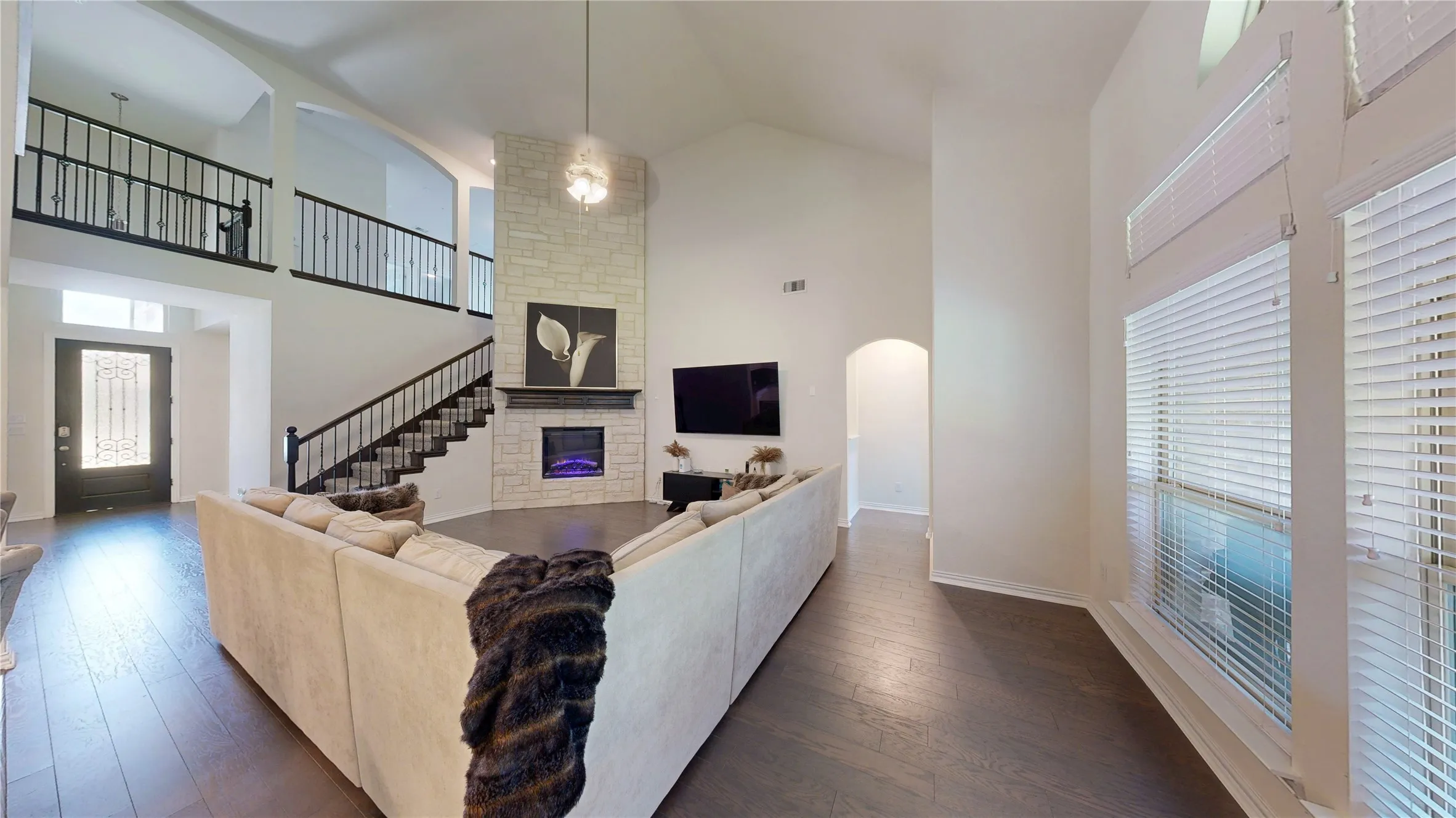 Spacious living area featuring high vaulted ceilings, wood-finish flooring, and a stone-clad fireplace with mantel