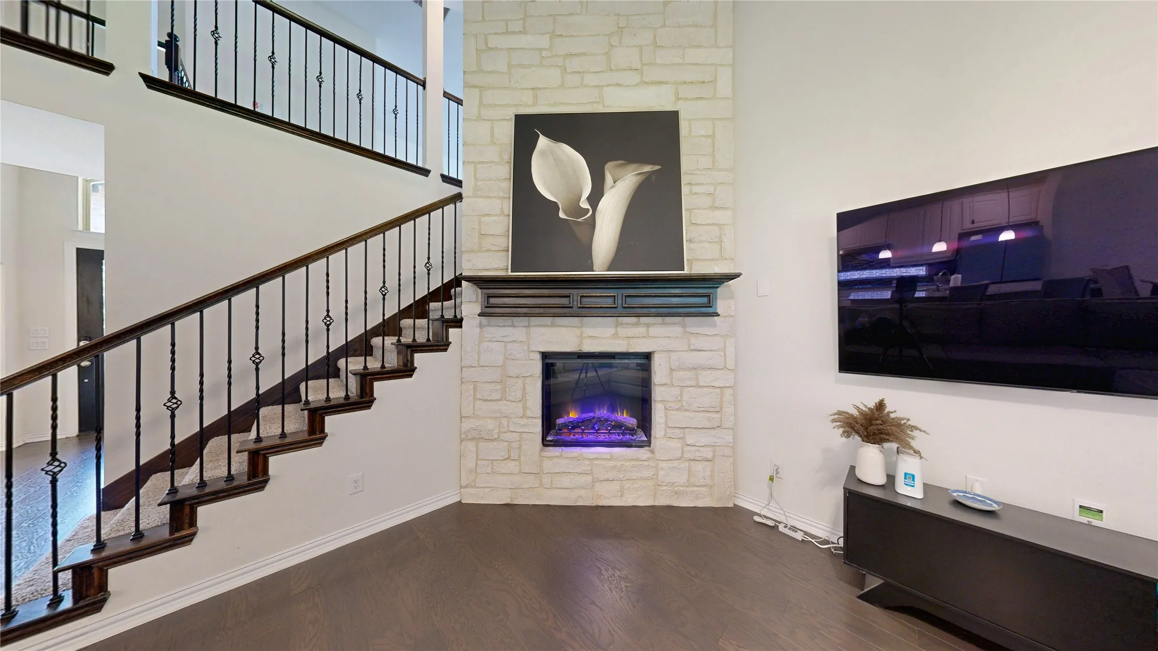 Staircase with dark wood treads and wrought iron balusters, complemented by a stone-clad fireplace featuring an electric insert and dark wood mantel