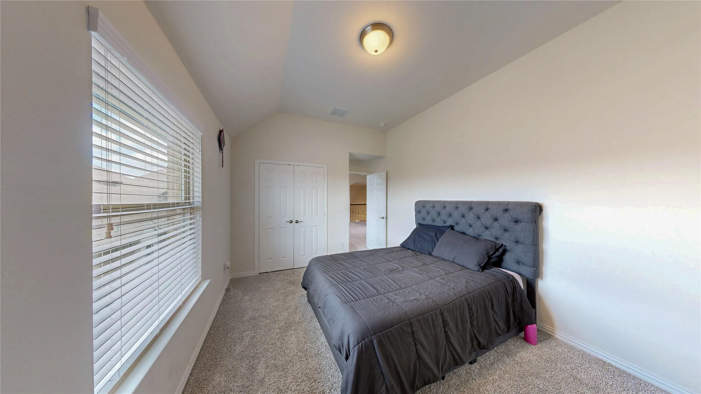Carpeted room with vaulted ceiling and a large window featuring horizontal blinds