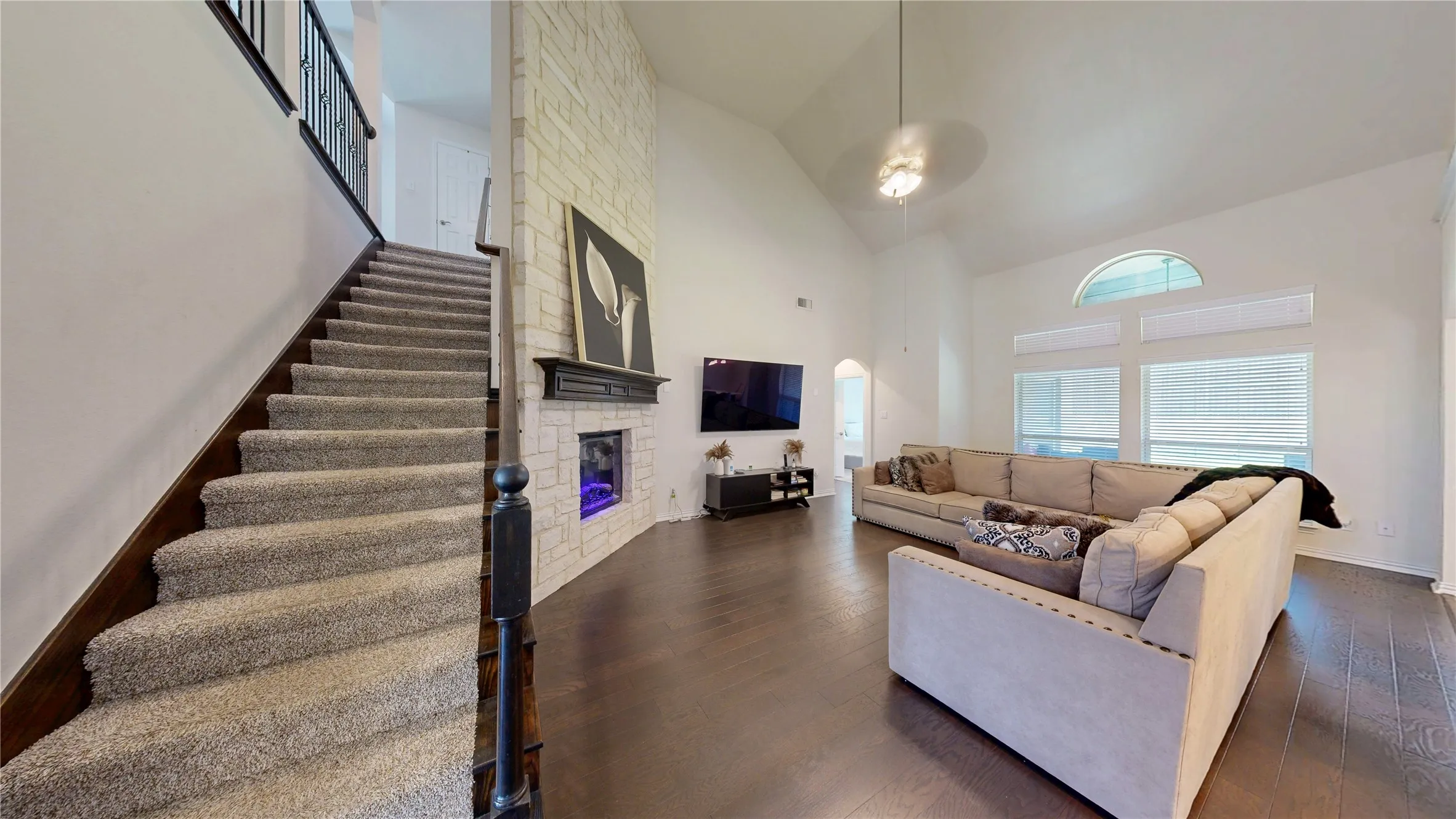 High vaulted ceilings enhance this living space featuring wood-finish flooring and a white stone-clad fireplace