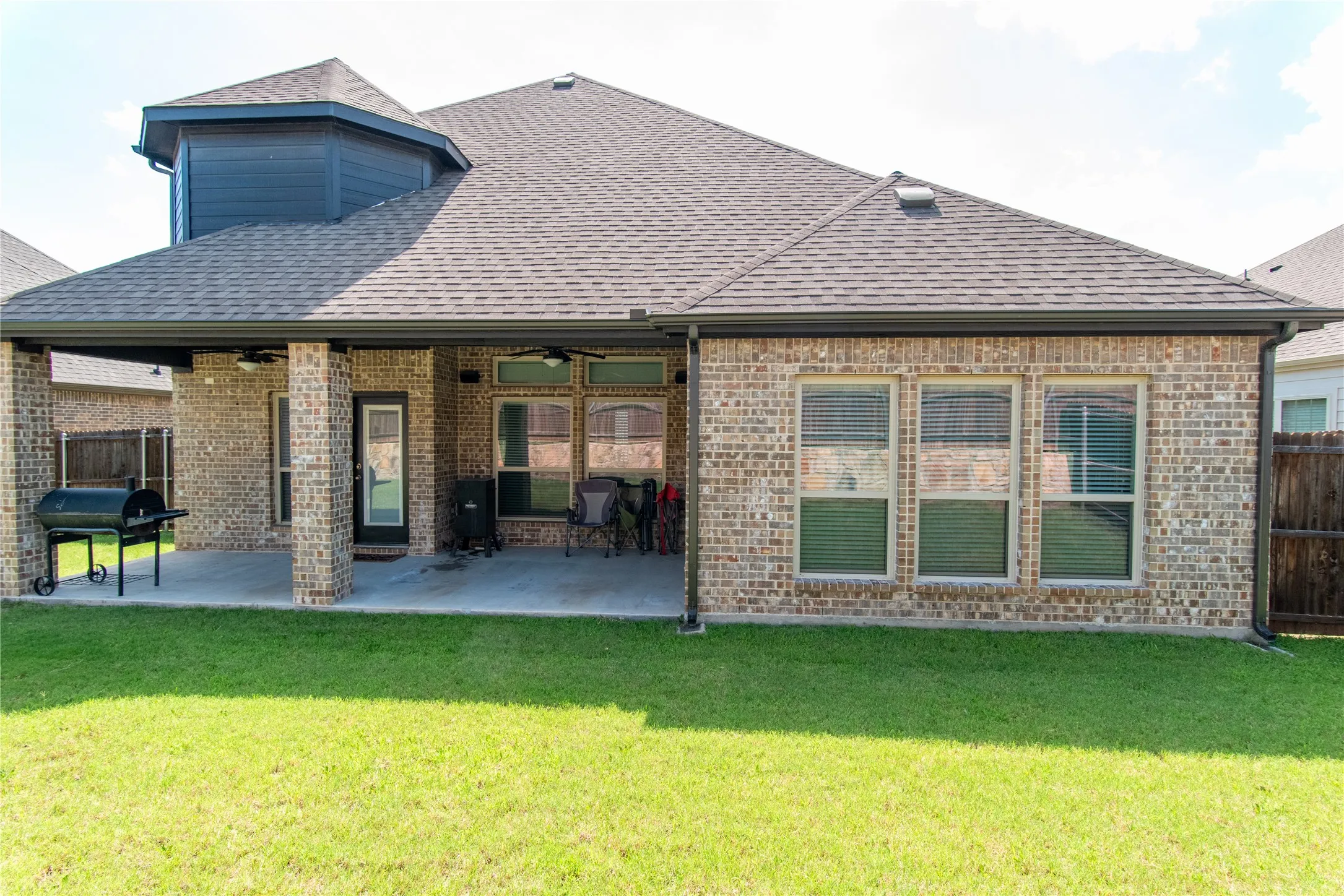 Expansive backyard featuring a covered patio with brick columns, ceiling fans, and a solid roofline