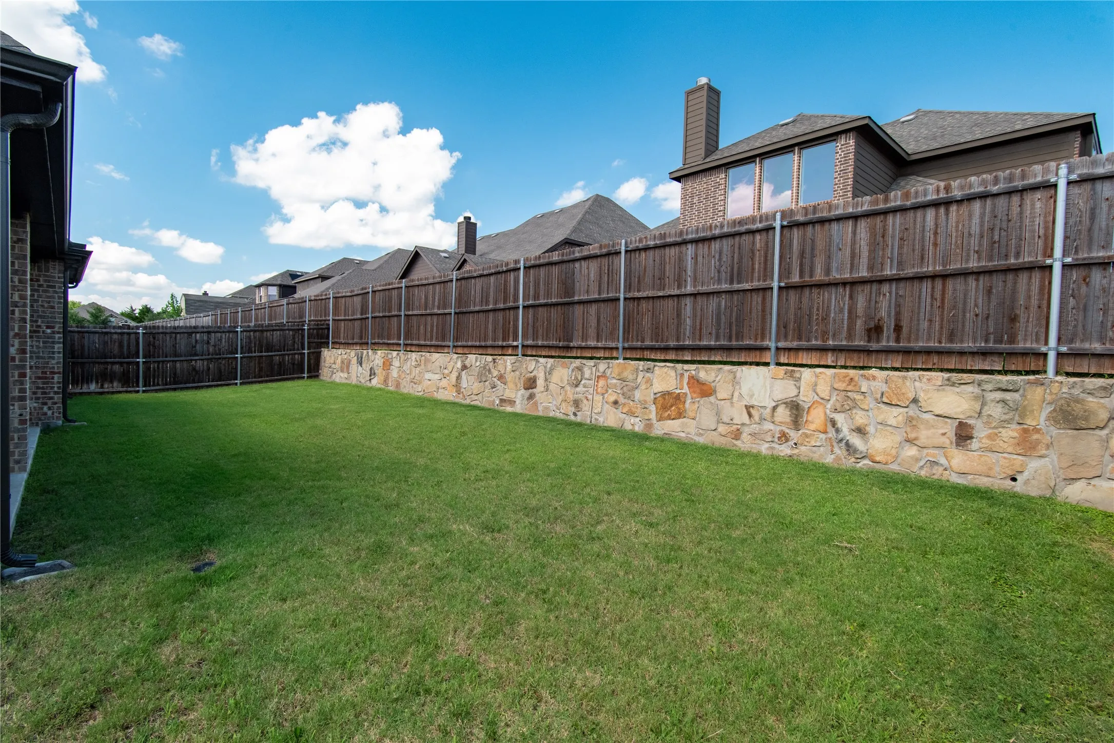 Expansive backyard featuring a lush lawn, a stone retaining wall, and a full privacy fence