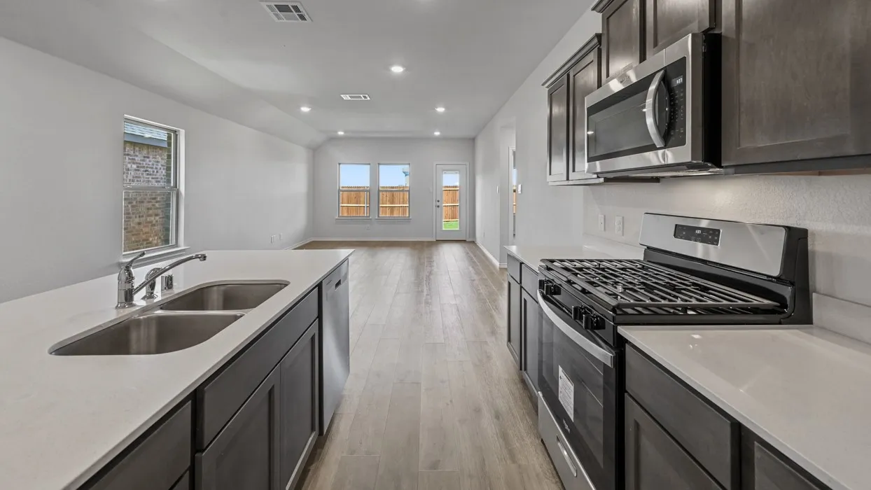 Open-concept kitchen featuring dark wood cabinetry, light countertops, a stainless steel gas range, a stainless steel over-the-range microwave, and wood-finish flooring
