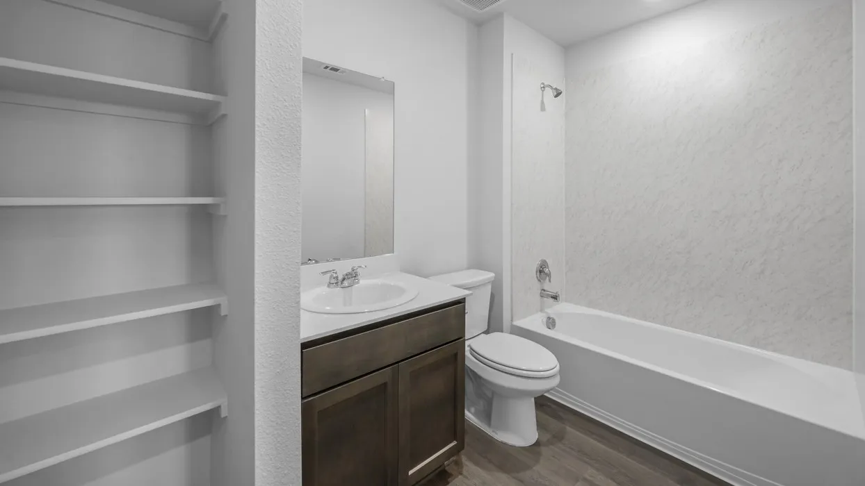 Full bathroom featuring a white bathtub with textured surround, a single vanity with a dark wood-finish cabinet, a white countertop, and a built-in shelving unit