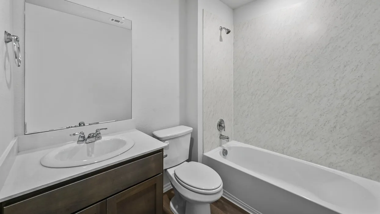Full bathroom featuring a single vanity with an integrated sink, a large wall-mounted mirror, a toilet, and a bathtub with a shower and patterned shower surround