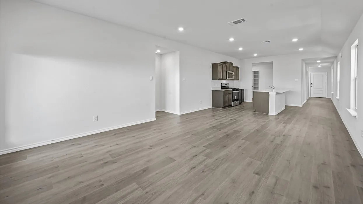 Expansive open-concept room featuring wood-finish flooring, recessed lighting, and a modern kitchen with dark cabinetry and stainless steel appliances