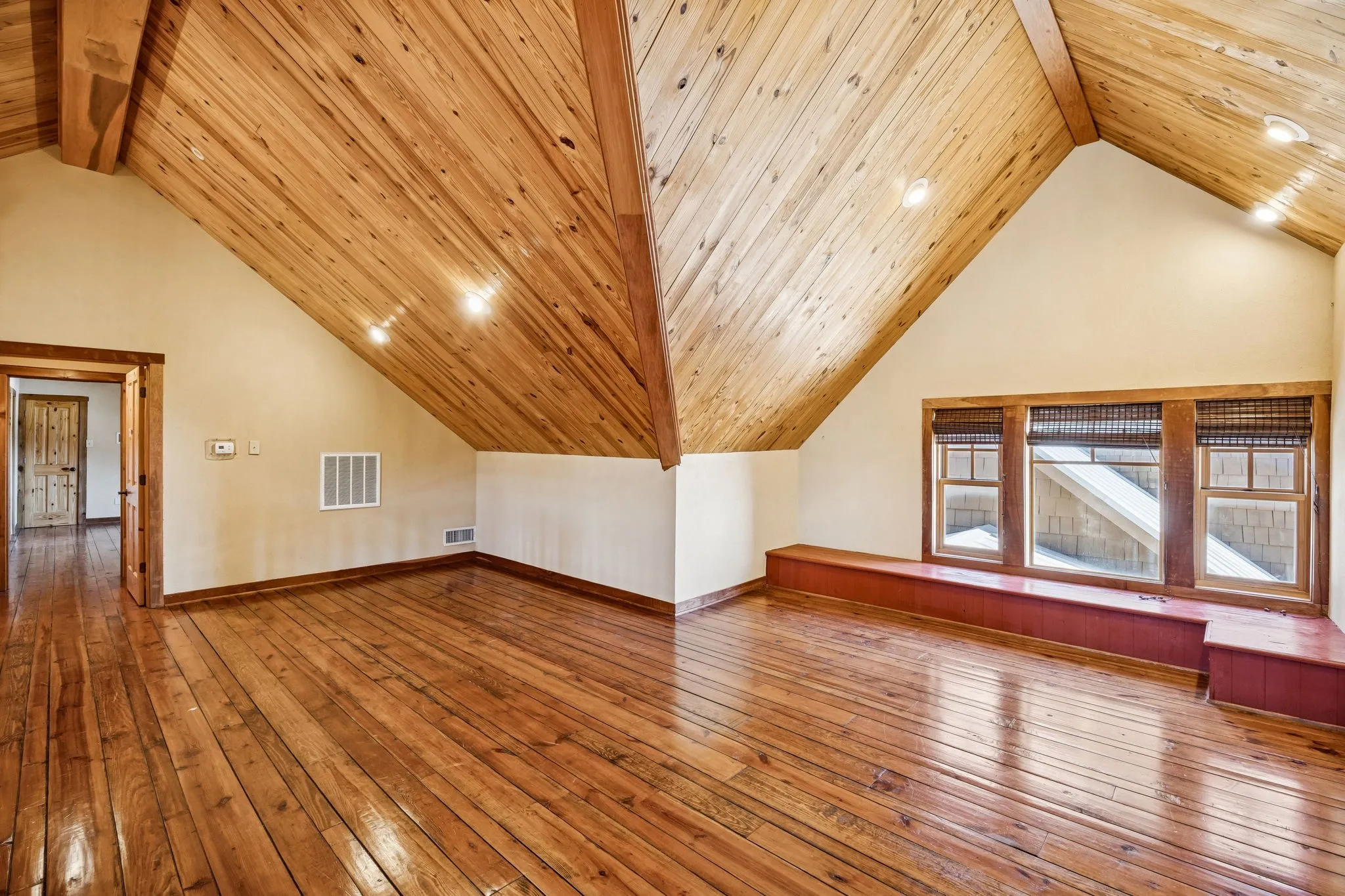 Spacious room featuring rich wood-finish flooring and a vaulted wood-paneled ceiling