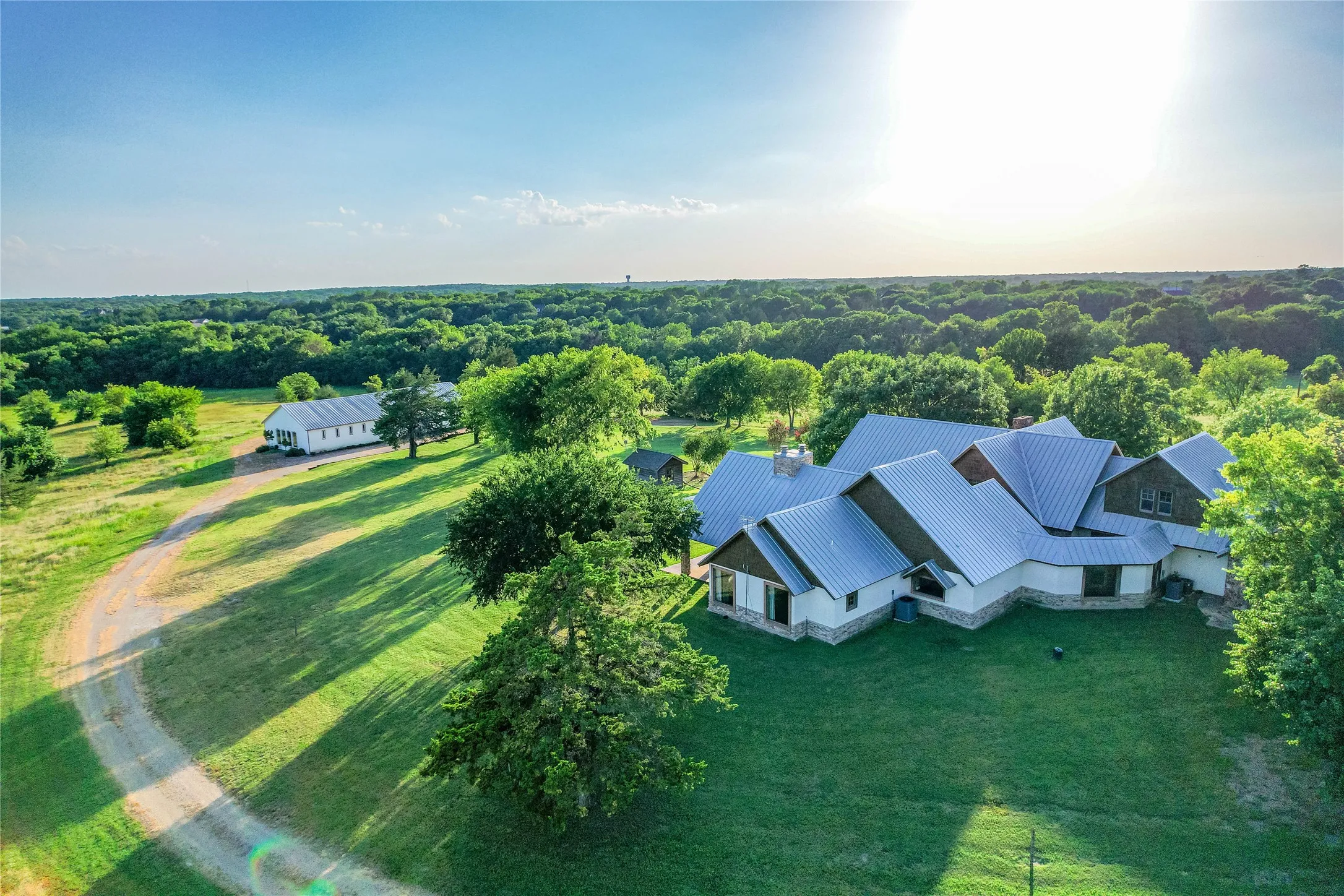 Expansive property featuring a multi-level residence with a metal roof and stone accents, surrounded by mature trees and manicured lawns