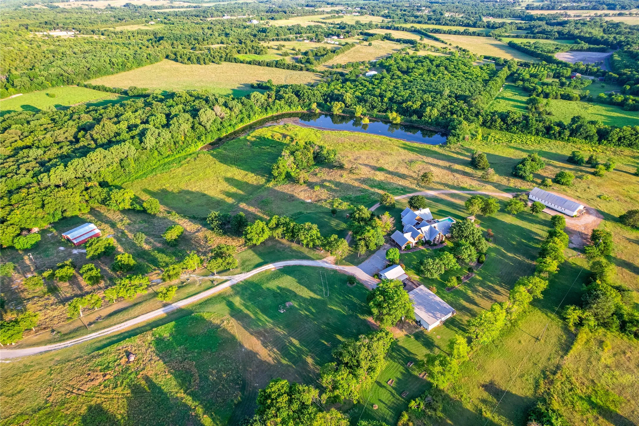 Expansive rural property featuring a main residence, multiple outbuildings, a pond, and extensive wooded areas