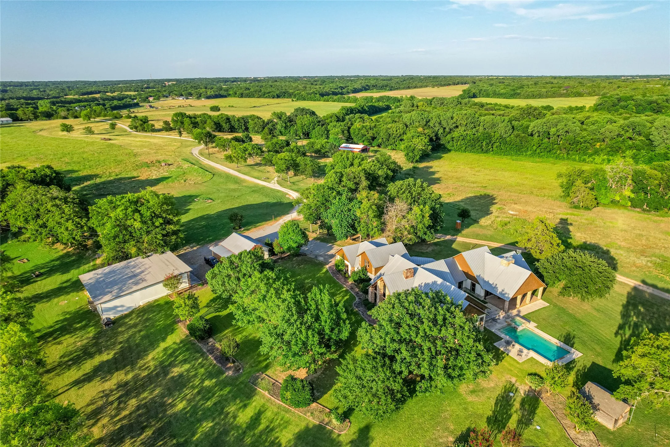 Expansive property featuring a main residence with a metal roof, a rectangular swimming pool, and multiple outbuildings