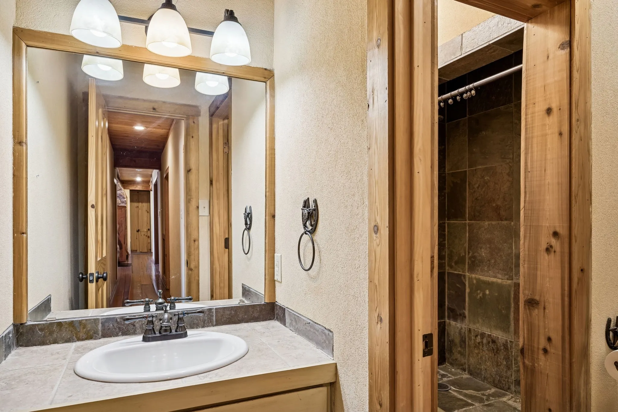 Bathroom vanity featuring a rectangular sink, dual-handle faucet, stone tile countertop, and wood-framed mirror