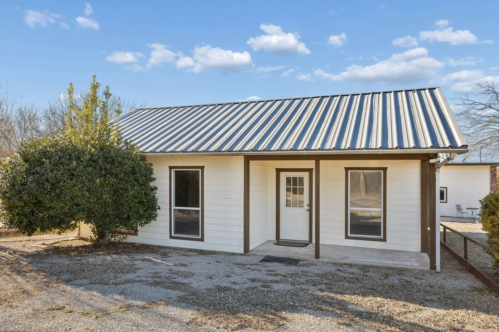 Exterior featuring white siding with brown trim, a metal roof, and a covered porch entry