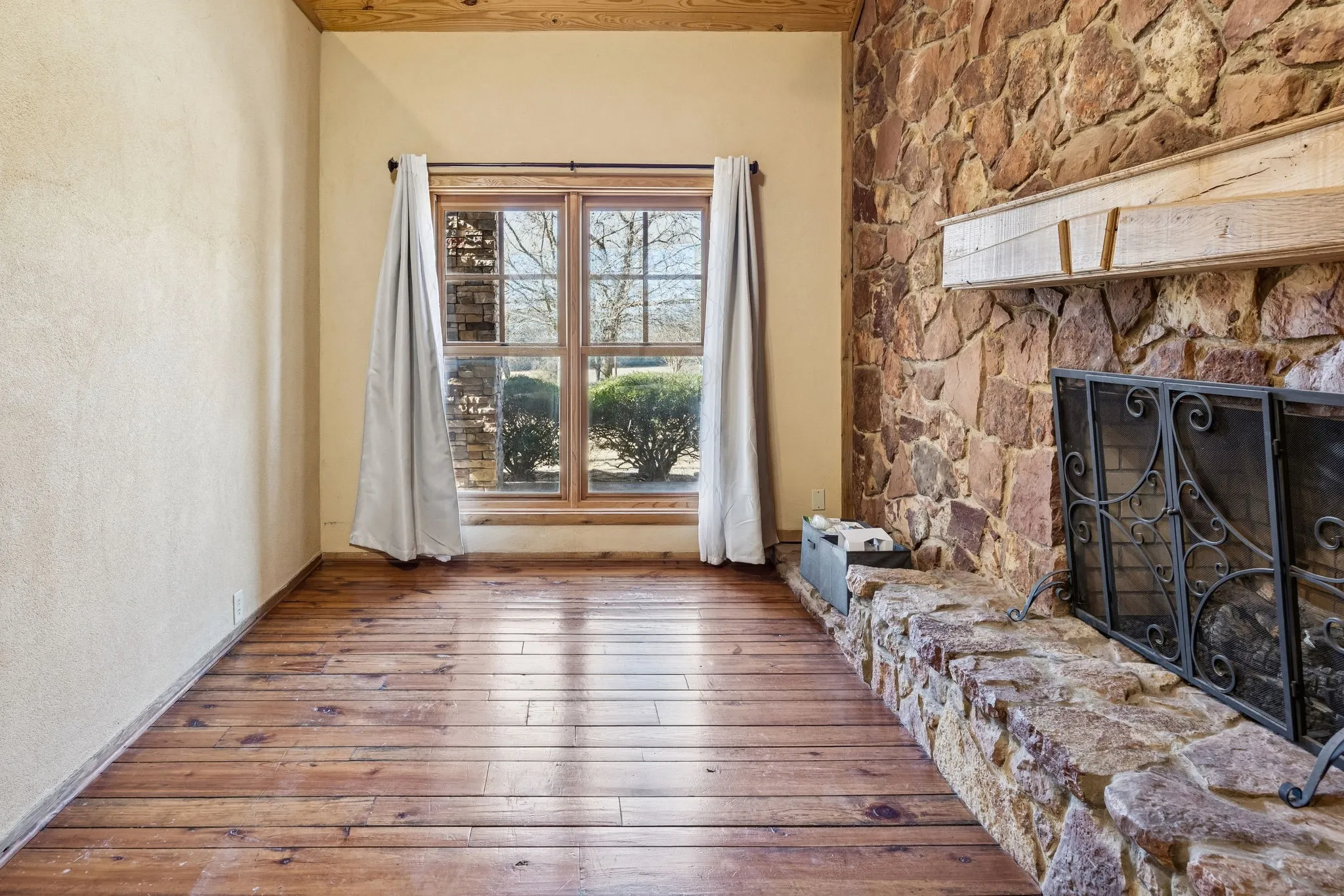 Wood-finish flooring throughout, featuring a stone fireplace with a wood mantle, and a large window with wood framing