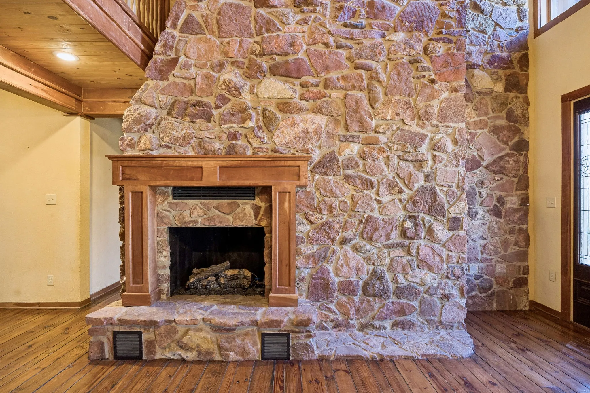 Floor-to-ceiling natural stone fireplace with a wood mantel