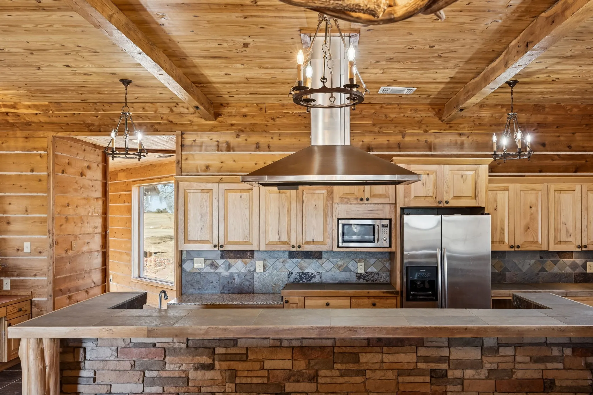 Kitchen featuring a stone-clad island with a composite countertop, wood cabinetry, a tile backsplash, and stainless steel appliances