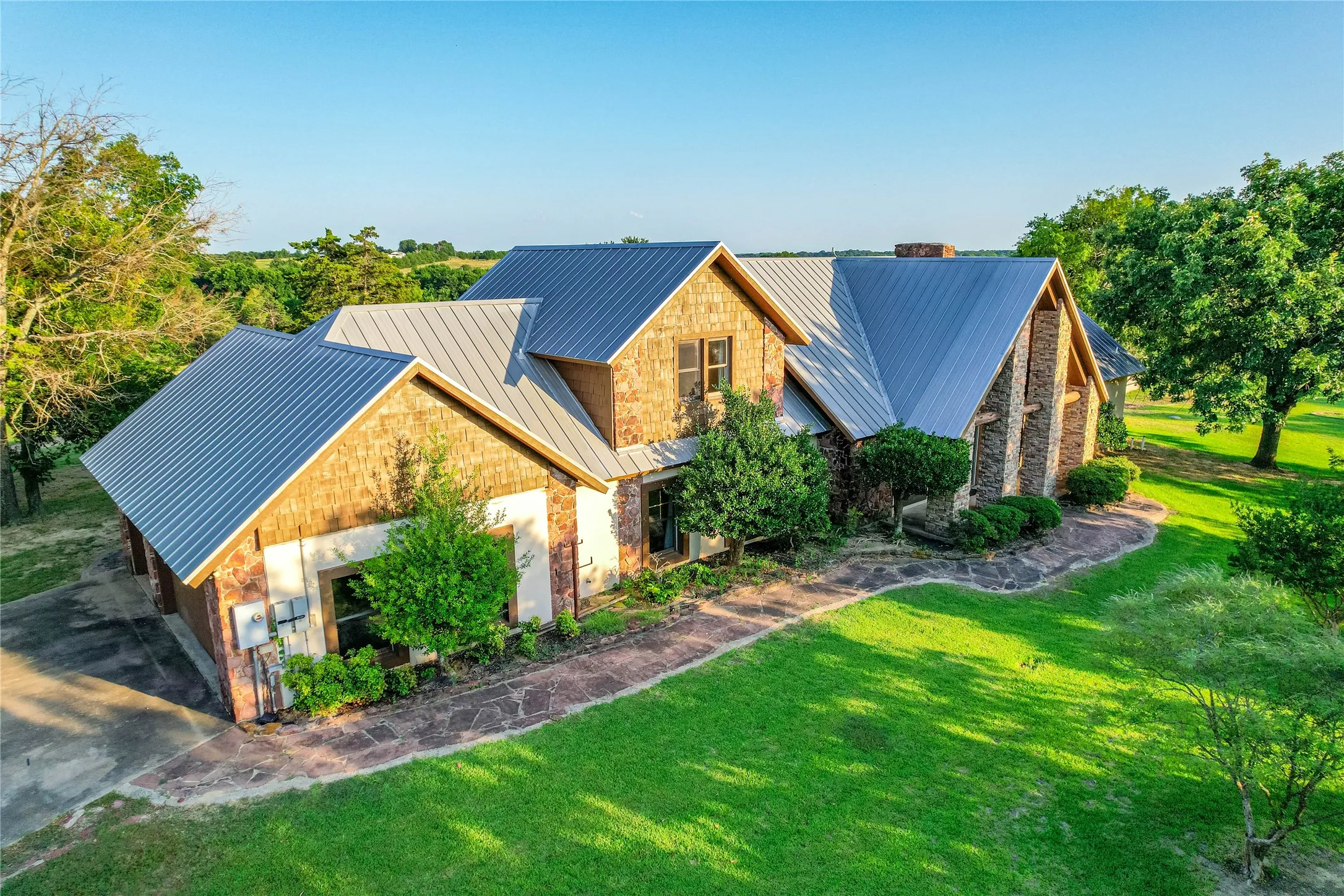 Stone and shingle exterior featuring a metal roof, extensive lawn, and mature landscaping