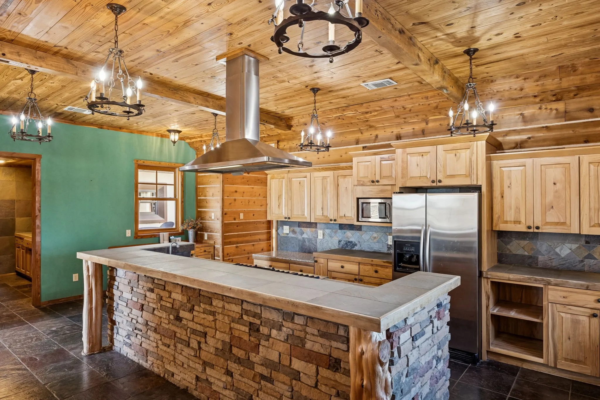 Kitchen featuring a stone-faced island with a tiled countertop, wood-finish cabinetry, and stainless steel appliances