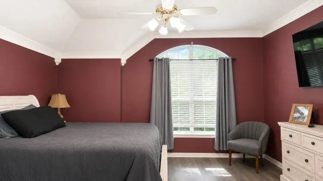 Vaulted ceiling with crown molding, ceiling fan with light fixture, arched window, wood-finish flooring, and built-in dresser