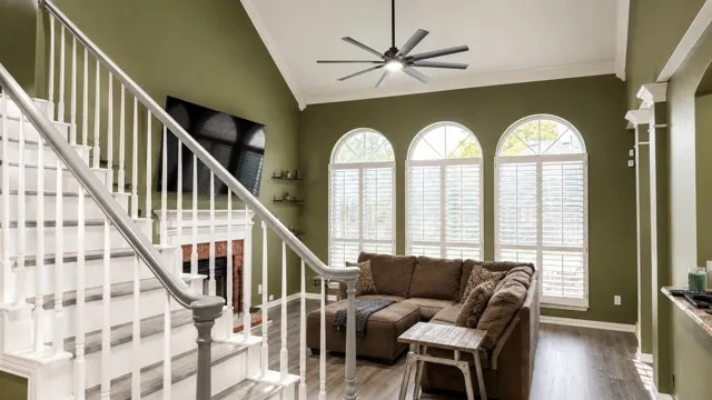 Living area featuring a vaulted ceiling with a modern ceiling fan, three arched windows with plantation shutters, a fireplace with a stone surround, wood-finish flooring, and a staircase with white risers and a gray handrail