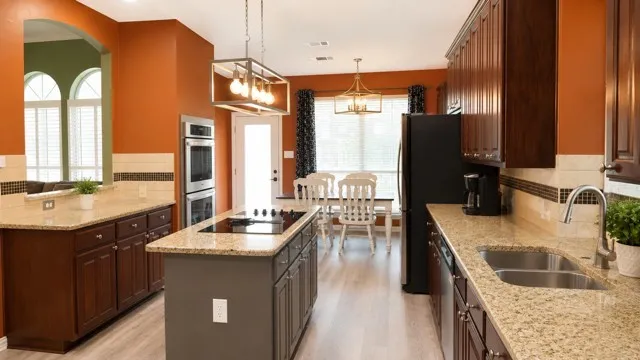 Kitchen featuring granite countertops, wood-finish flooring, dark wood cabinetry, a center island with cooktop, and stainless steel double ovens