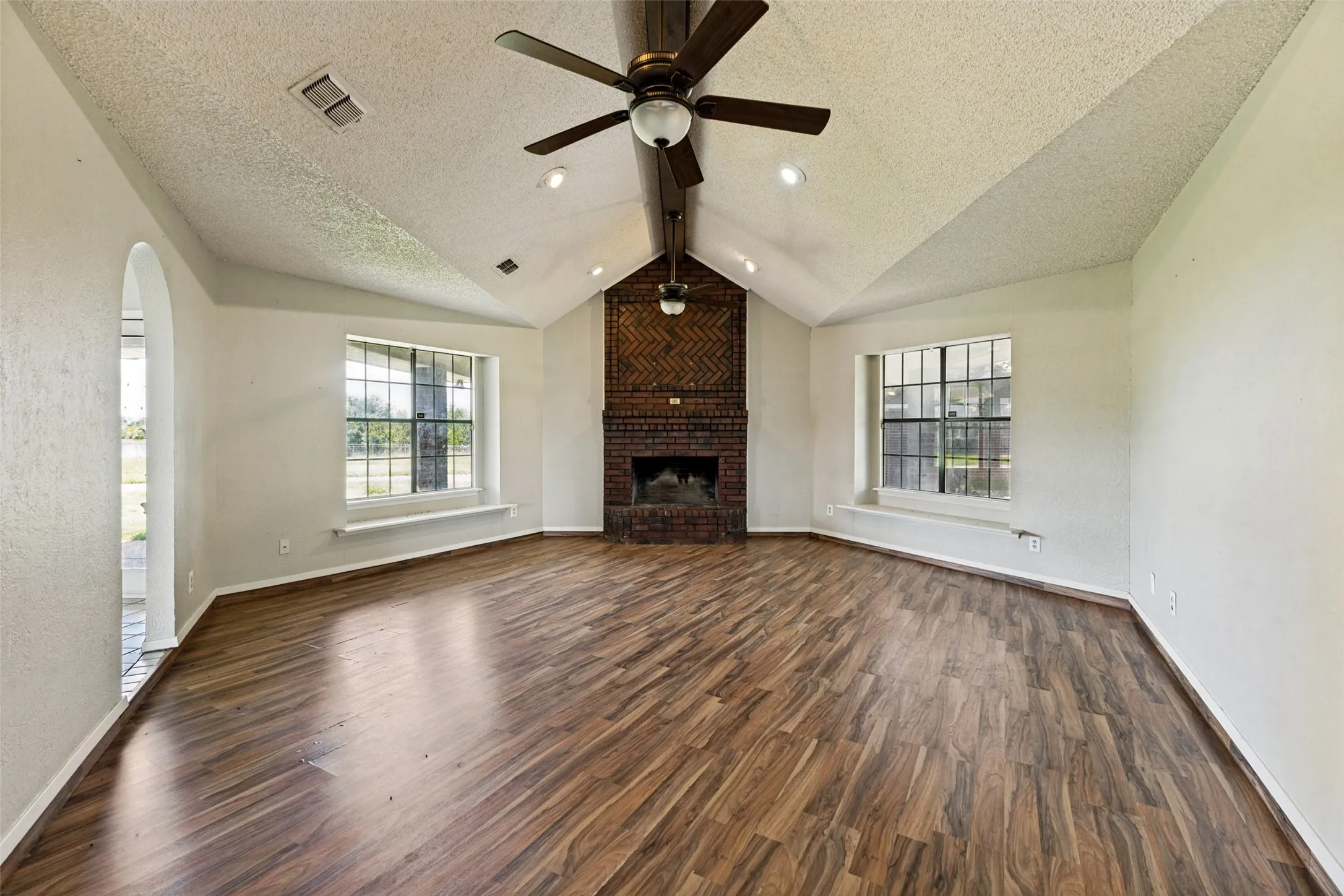 Spacious family room with would look laminate, brick wood-burning fireplace & vaulted ceiling (2nd home)