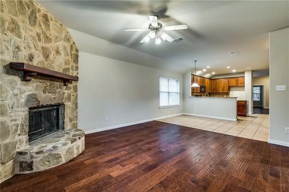 Living area with a stone fireplace featuring a wood mantel, wood-finish flooring, and a ceiling fan