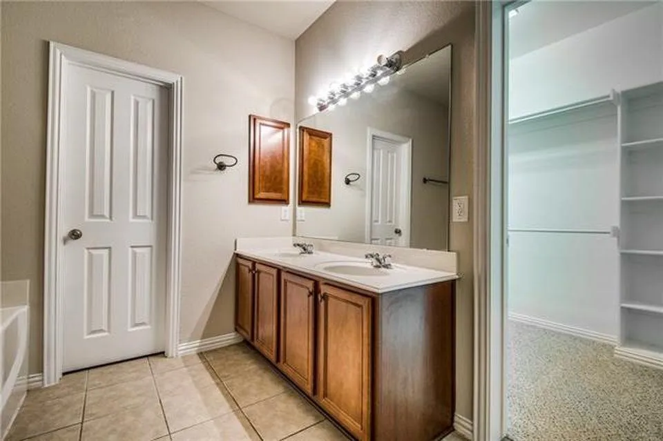 Bathroom featuring a dual-sink vanity with wood cabinetry, a large mirror, and tile flooring