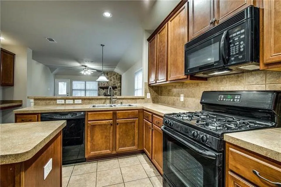 Kitchen featuring wood cabinetry, stone-look countertops, tile backsplash, and a black appliance suite with a gas range and built-in microwave