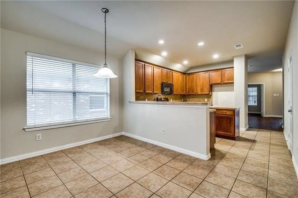 Kitchen and dining area featuring tile flooring, wood cabinetry, recessed lighting, a window with blinds, and a pendant light fixture