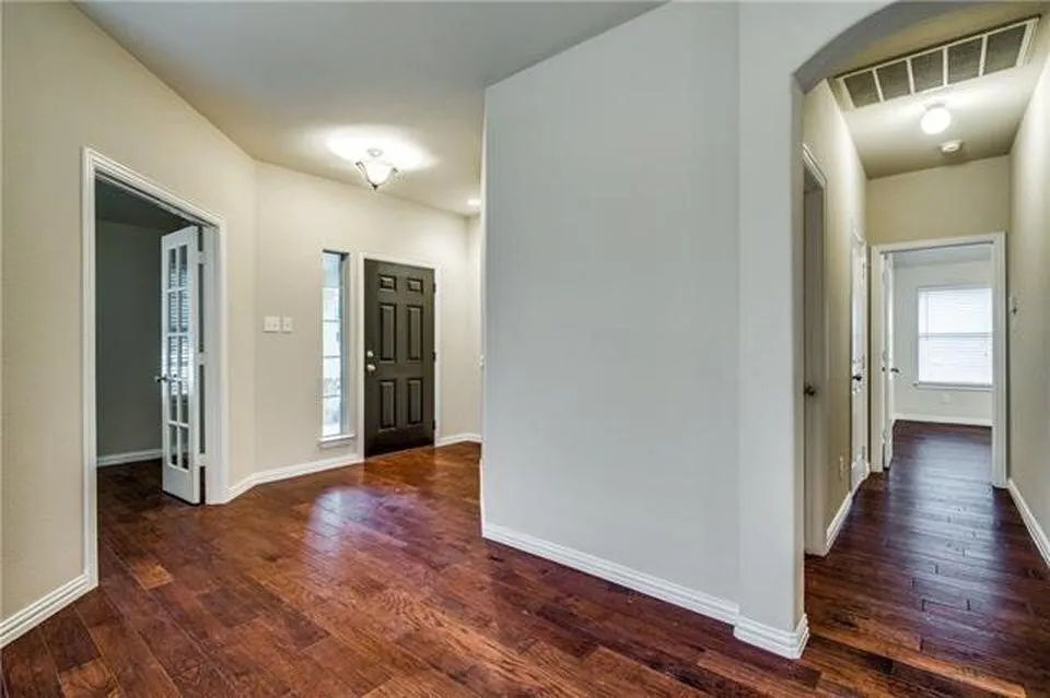 Entryway featuring rich wood-finish flooring, a dark paneled front door with sidelight windows, a ceiling-mounted light fixture, and an interior French door