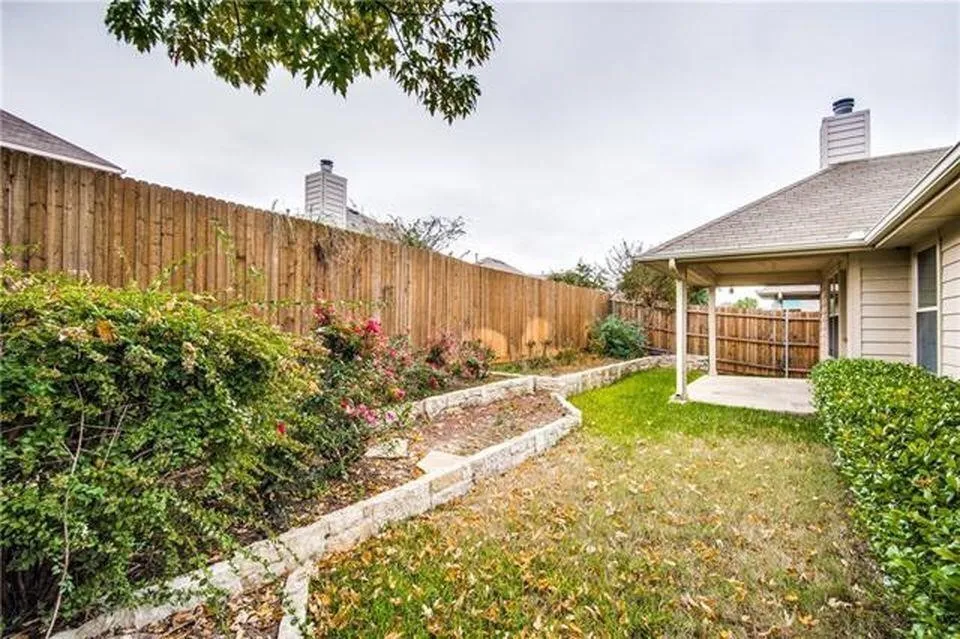 Private backyard featuring a covered patio, wood privacy fence, and stone-edged planting beds