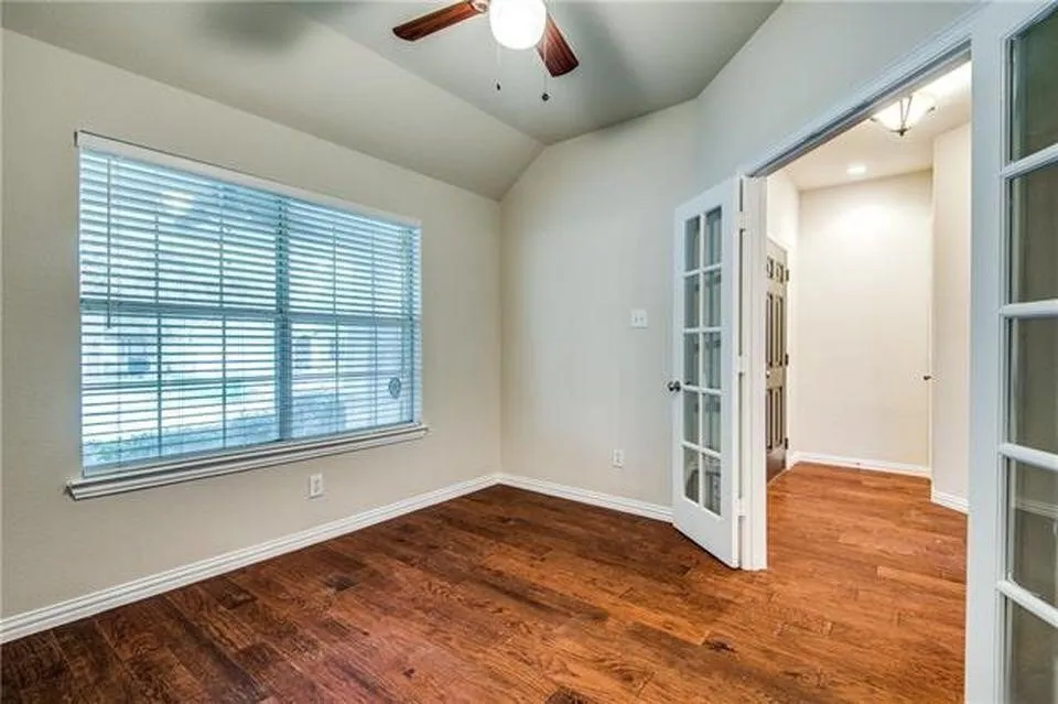 Room featuring wood-finish flooring, a large window with horizontal blinds, and a ceiling fan with light fixture