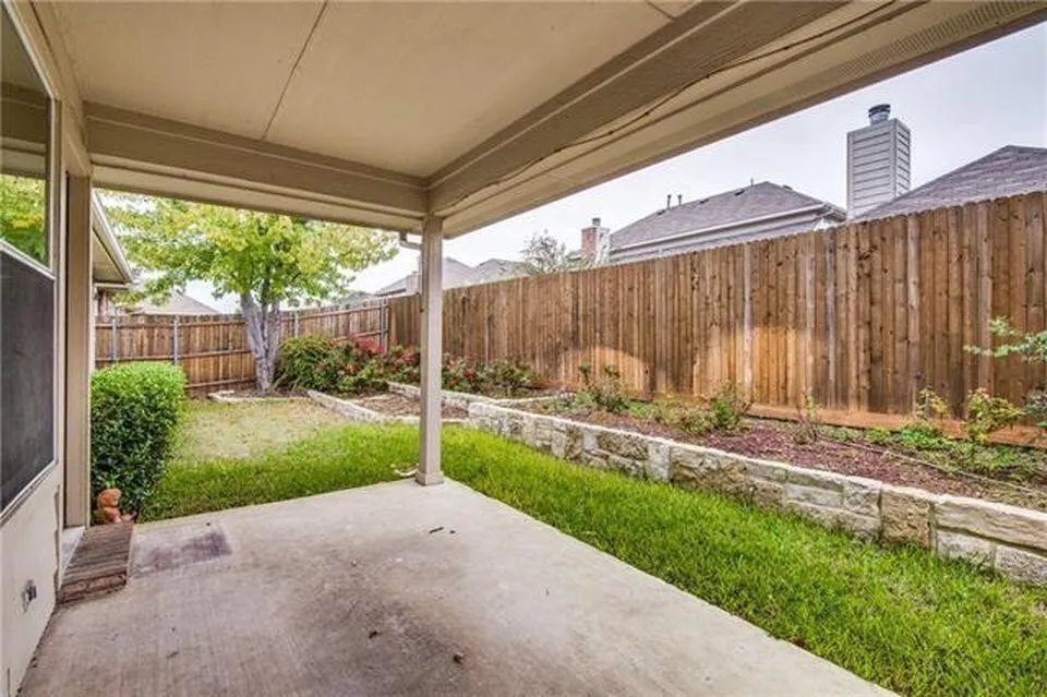 Covered patio featuring a concrete surface, a manicured lawn, and stone-edged garden beds