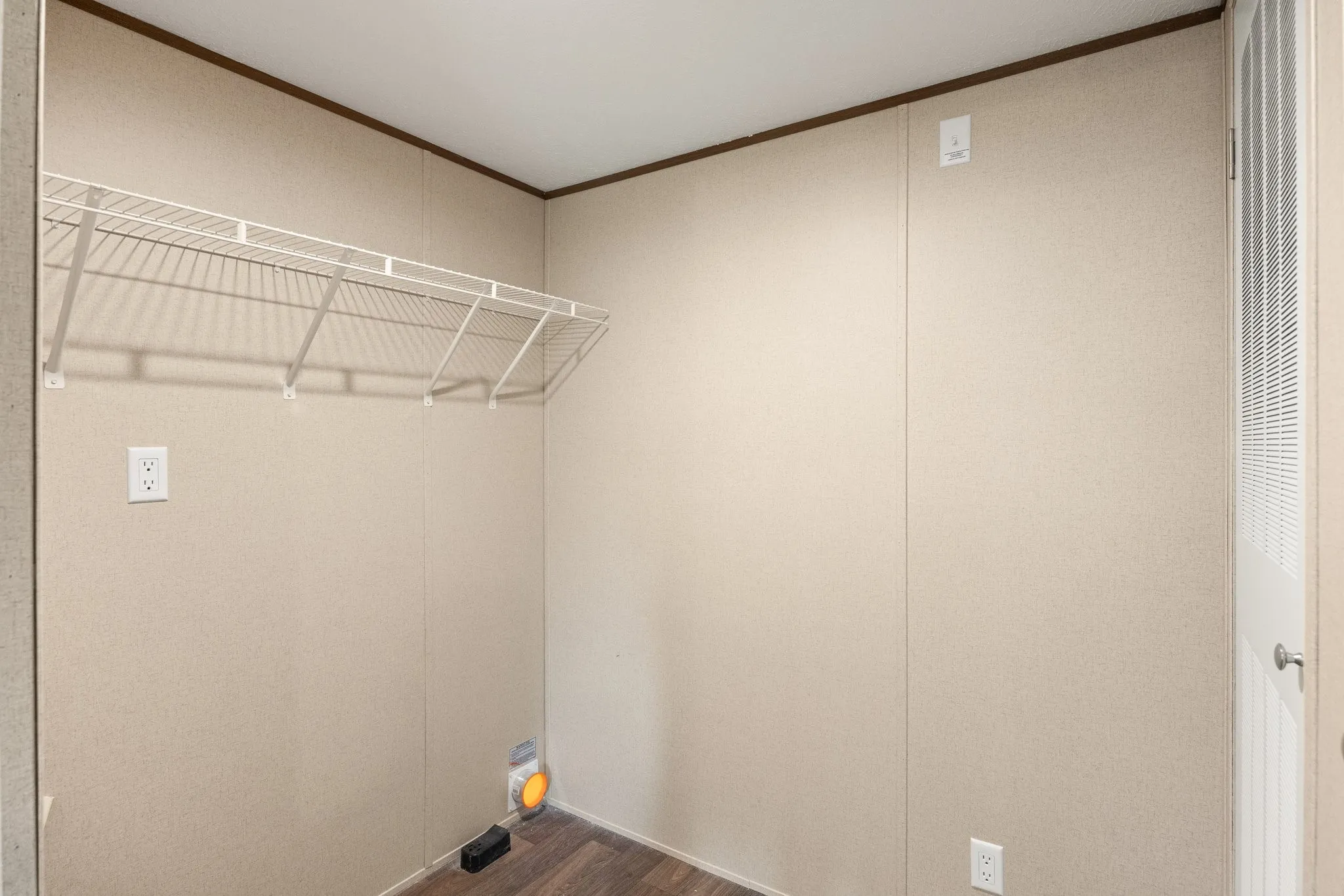Utility area featuring wire shelving, wood-finish flooring, a louvered door, and wall outlets