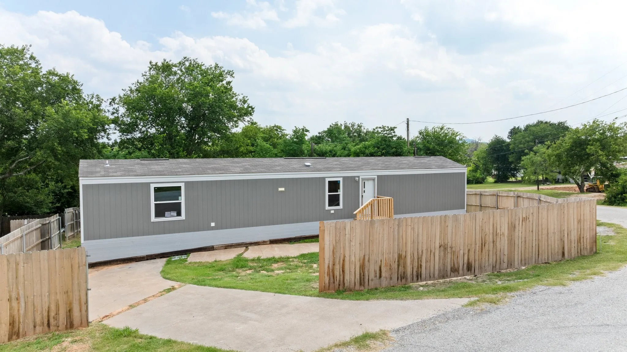 Contemporary modular home featuring gray siding, a privacy fence, concrete drive, and a front entry with wooden steps