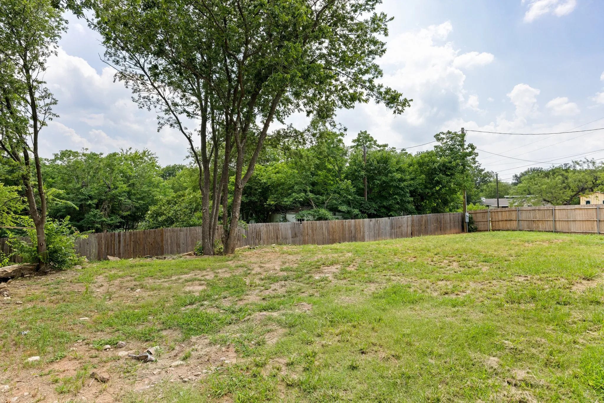Expansive outdoor space featuring a wood privacy fence, mature trees, and a spacious lawn