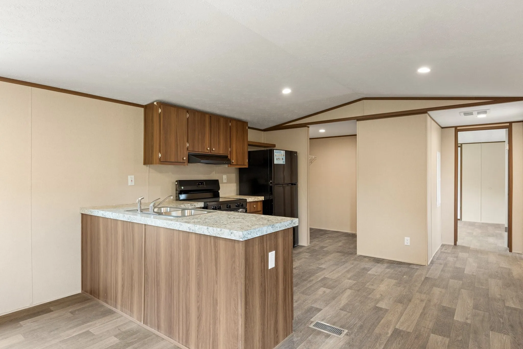 Kitchen area featuring wood-finish flooring, a kitchen island with a double basin sink and light-toned countertop, wood cabinetry, and black appliances including a range and refrigerator