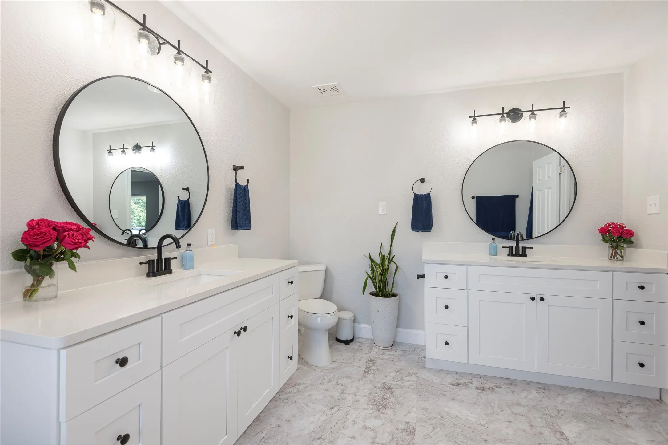 Spacious bathroom featuring dual white vanities with quartz countertops, matte black fixtures, round mirrors,
