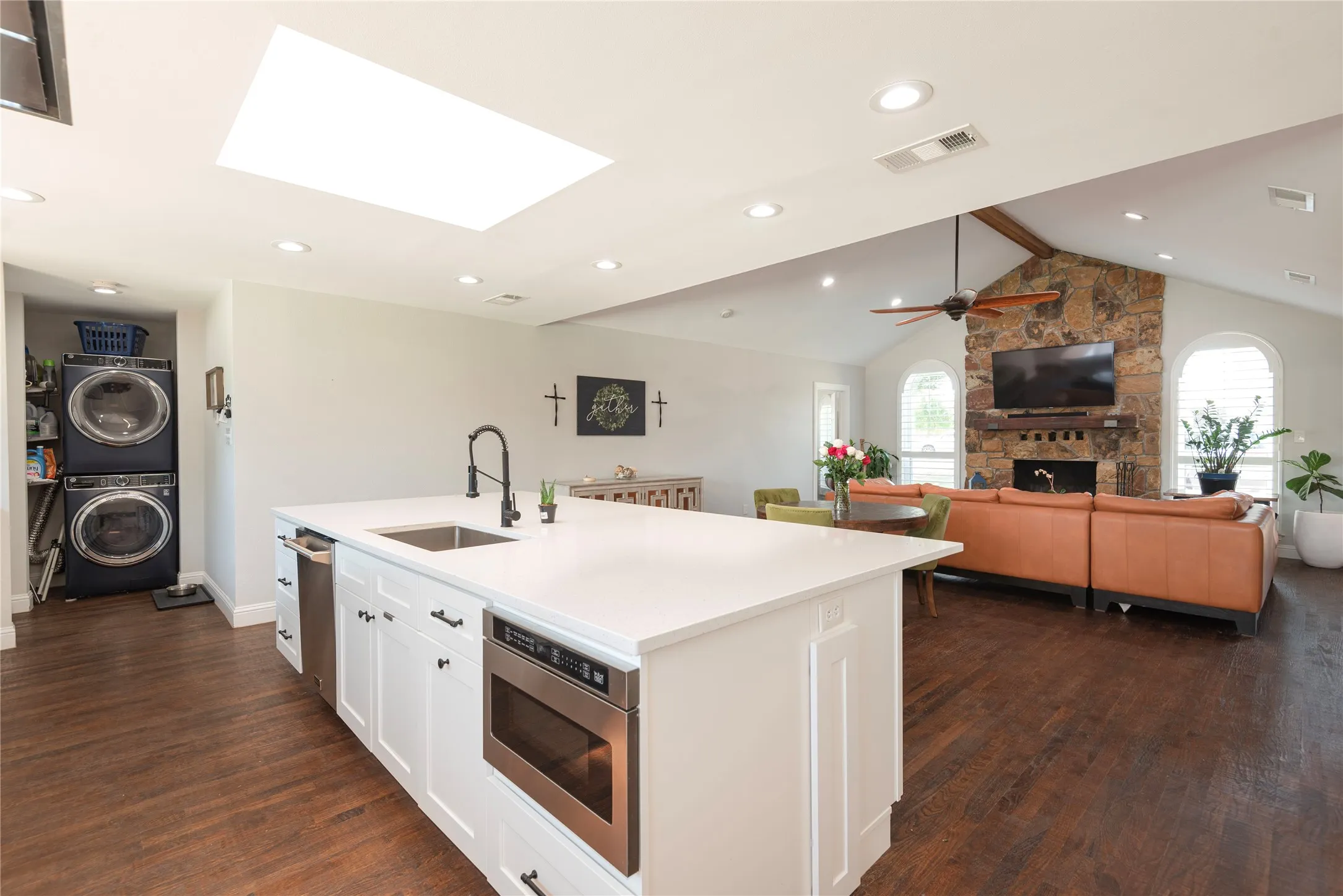 Kitchen island with 360 cabinetry, featuring a stainless steel sink with a matte black faucet, integrated microwave, and dishwasher, stacklaundry