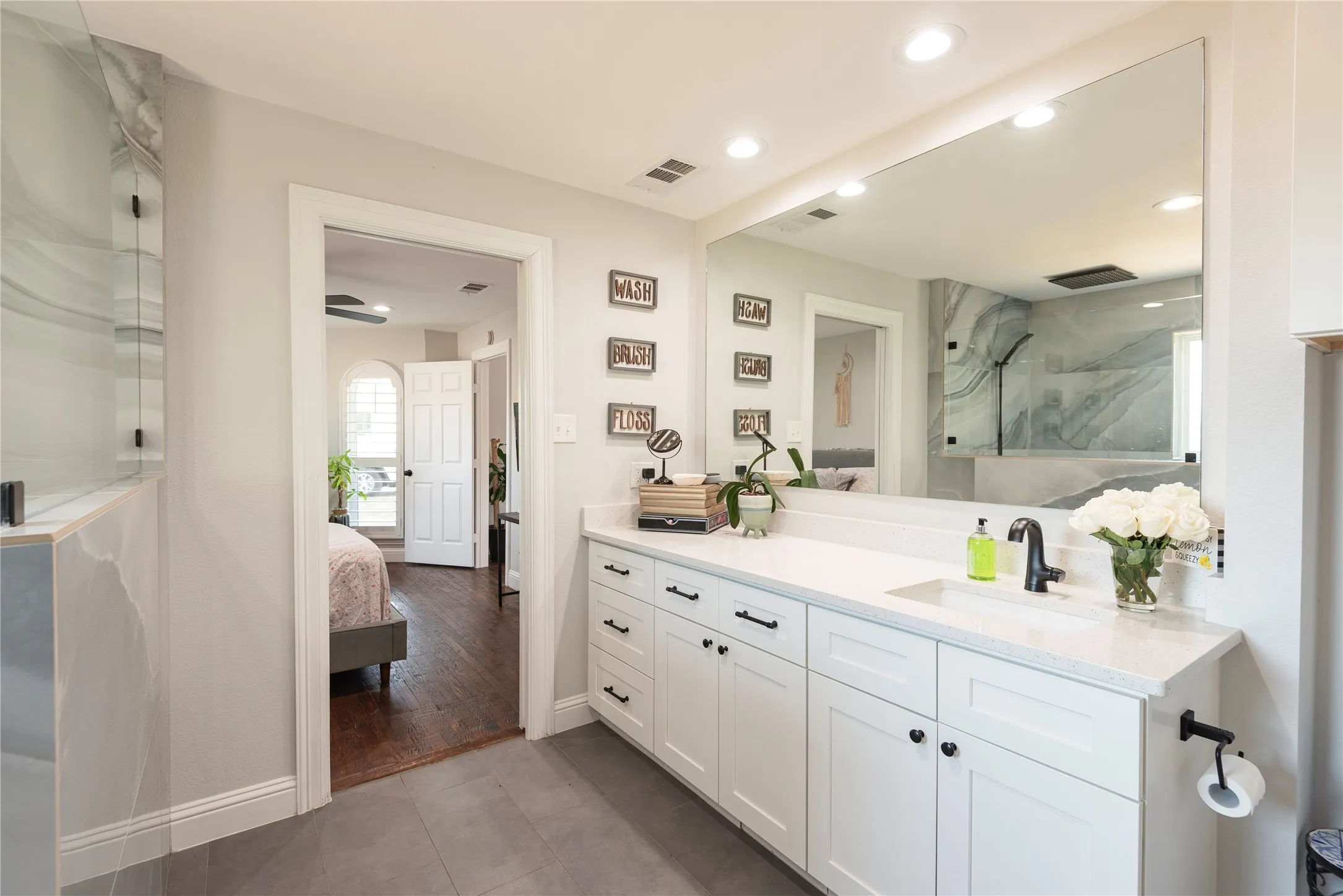 Vanity featuring a quartz countertop with an undermount sink, white cabinetry with black hardware, and an expansive wall-mounted​​‌​​​​‌​​‌‌​‌‌​​​‌‌​‌​‌​‌​​​‌​​ mirror