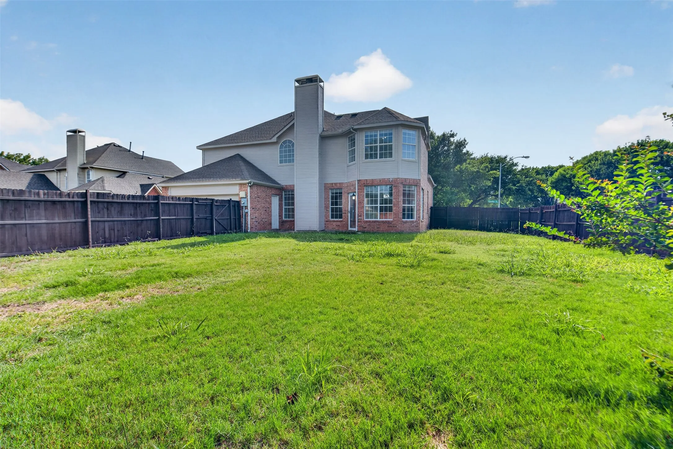 Spacious backyard with a partial brick and siding exterior, featuring multiple windows, a prominent chimney, and a privacy fence